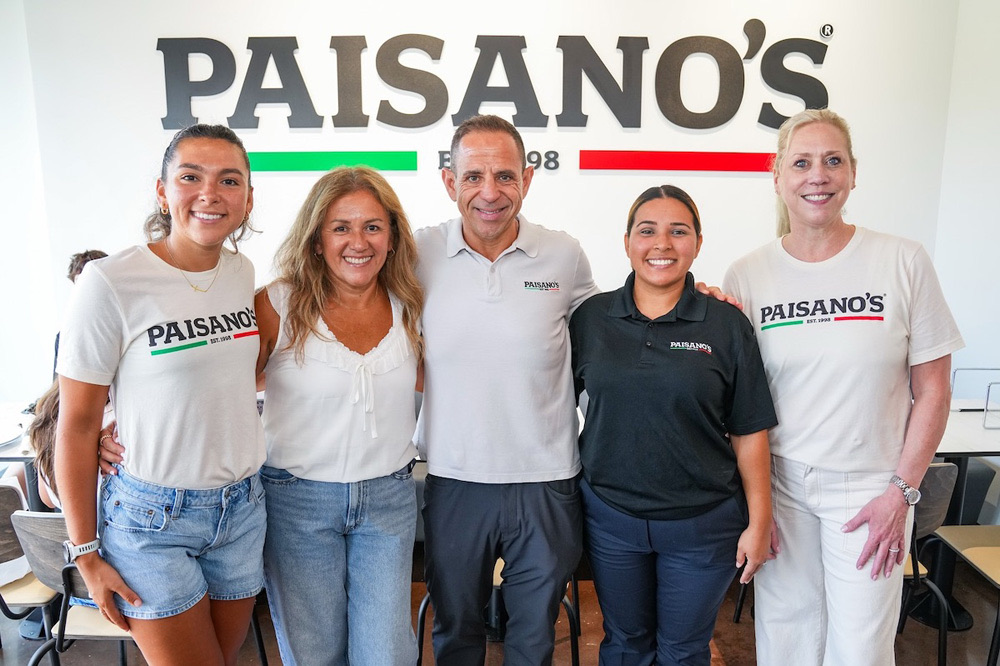 The Paisano’s team in front of the Paisano’s logo wall